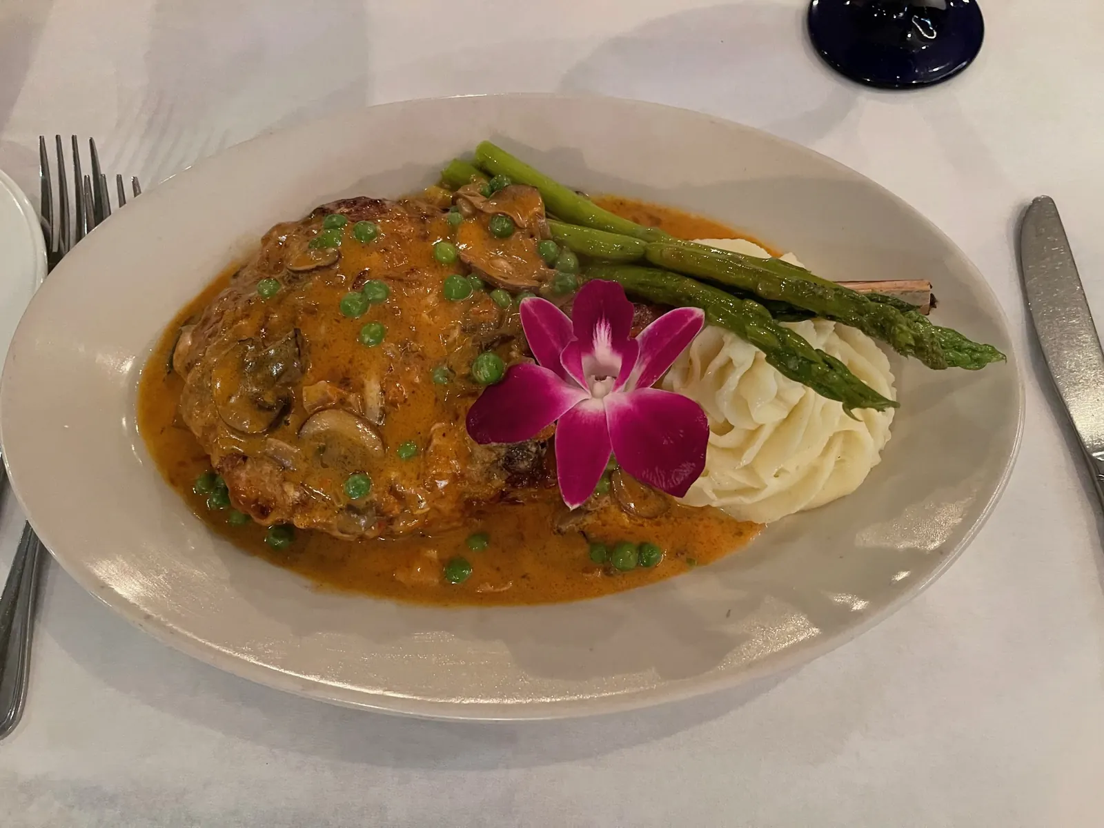 An entrée with asparagus and mashed potatoes, garnished with an orchid